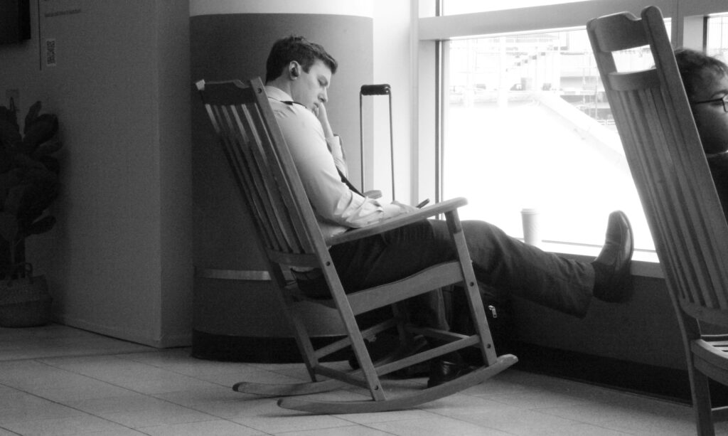 Black and white photo of a man resting in a rocking chair at an airport window.