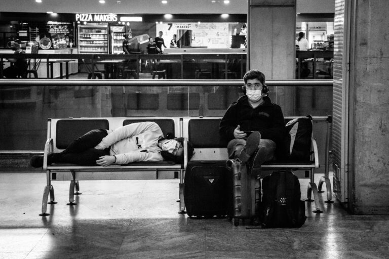 Two people resting in an airport, capturing the pandemic's impact on travel.