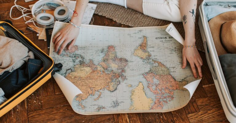 A traveler plans a journey, sitting on the floor with a world map and suitcase filled with essentials.